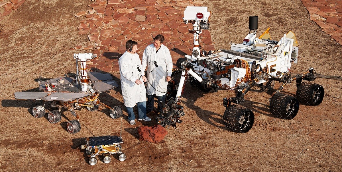 Two JPL engineers are standing next to three different generation vehicles from Mars Rovers